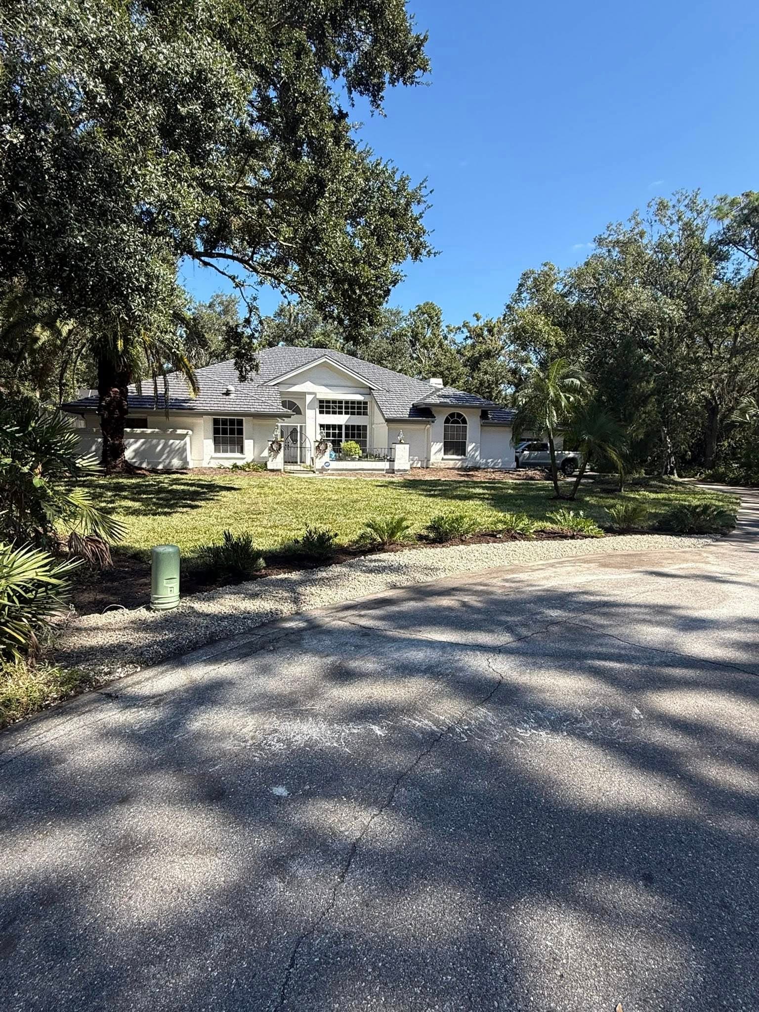 Single-story gray house with a landscaped yard, surrounded by trees and a clear blue sky.